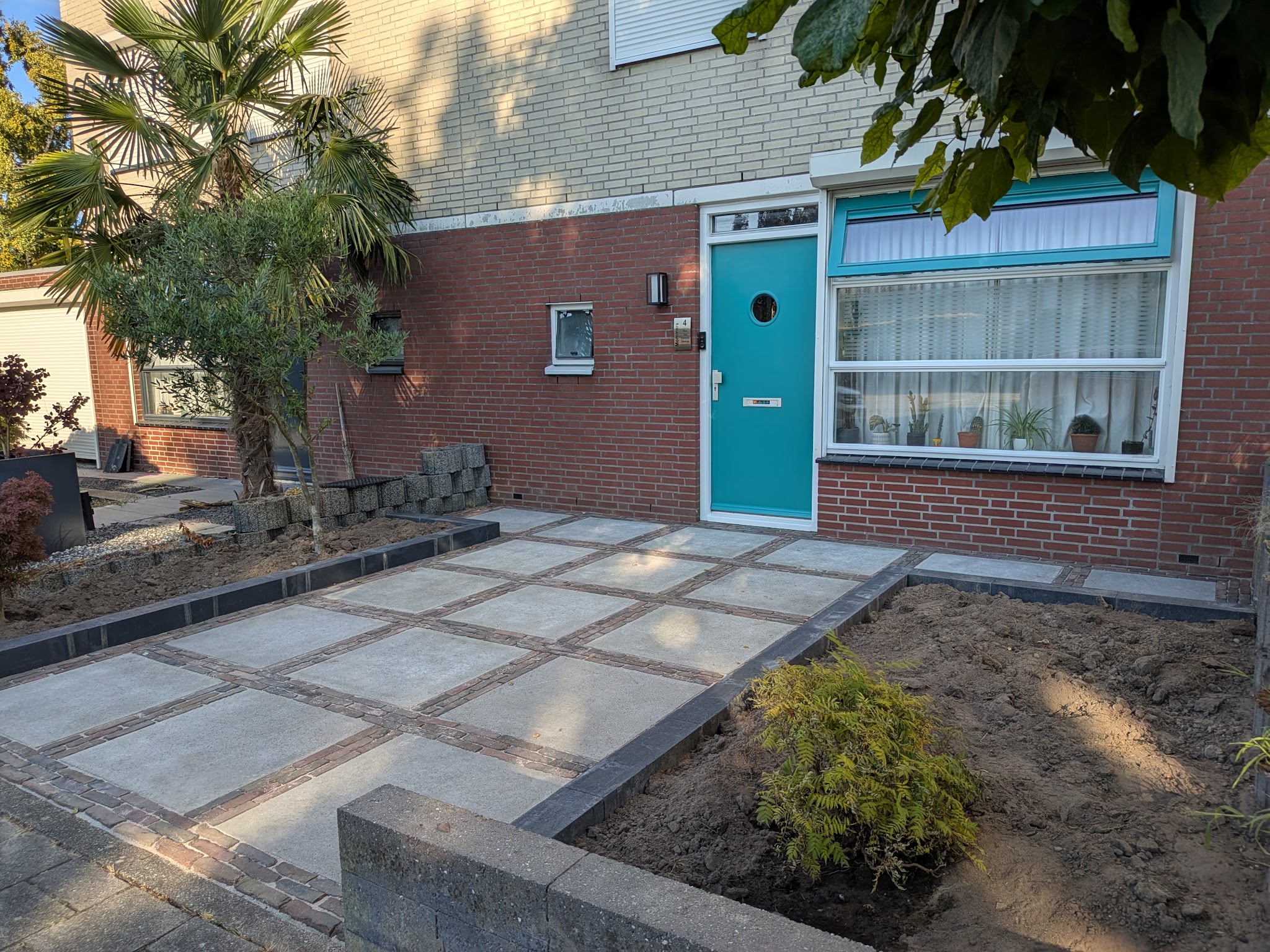 Voortuin tijdens de aanleg: nieuwe tegels met banden van oude klinkers