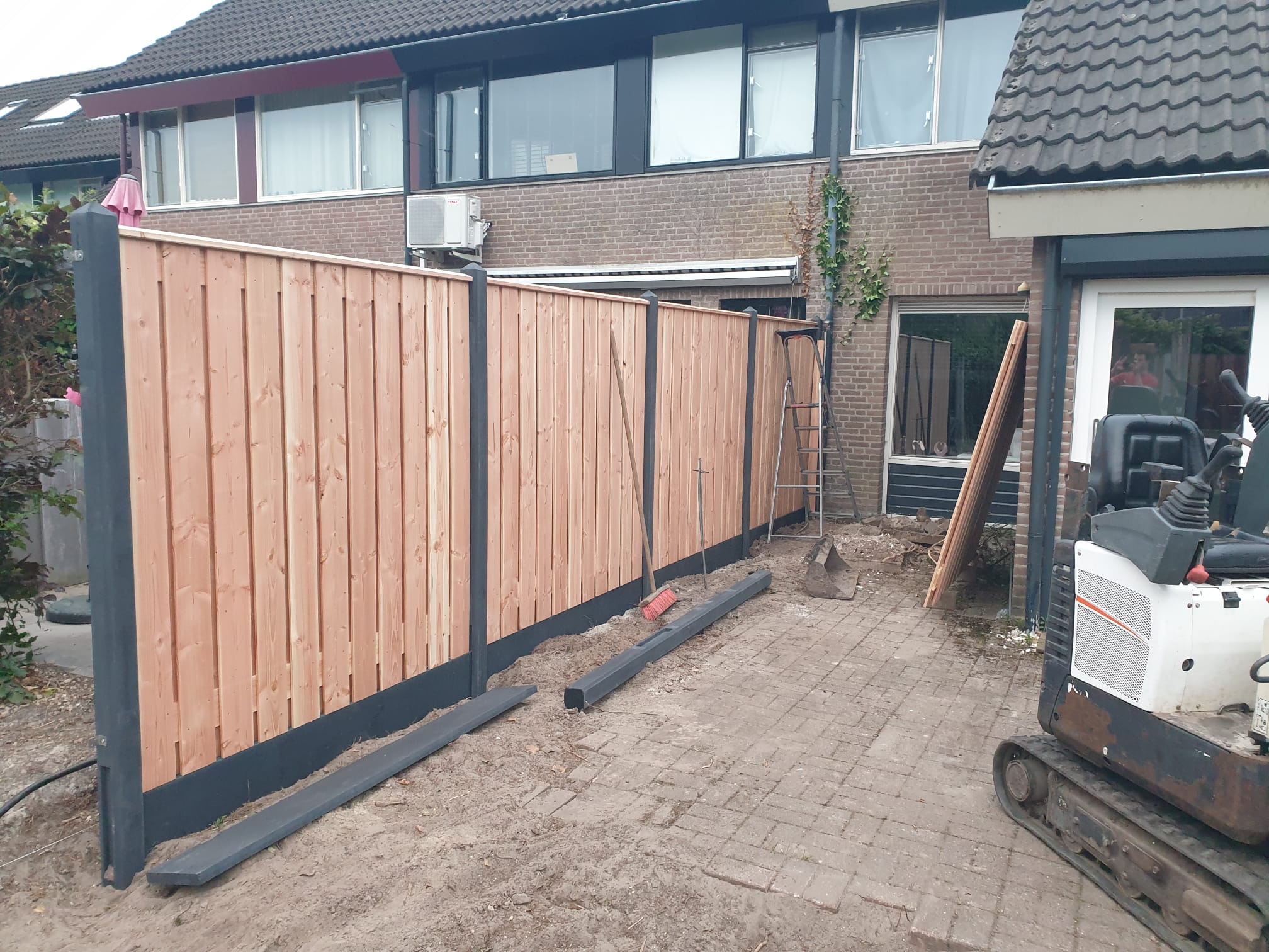 Nieuwe schutting van hout met betonnen palen, met een minigraver in de tuin